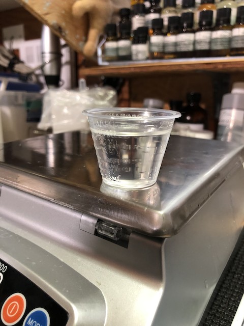 A cup of clear liquid sits on the edge of the metal plate on a digital scale. This is Cation G16S