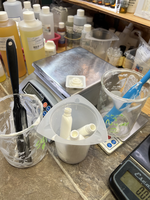 A photo of three containers after packaging a cold process emulsion using SEPILIFE™ NUDE. The first beaker contains a bit of lotion with a black spatula. The second contains three small tottle bottles. The third has a blue spatula.