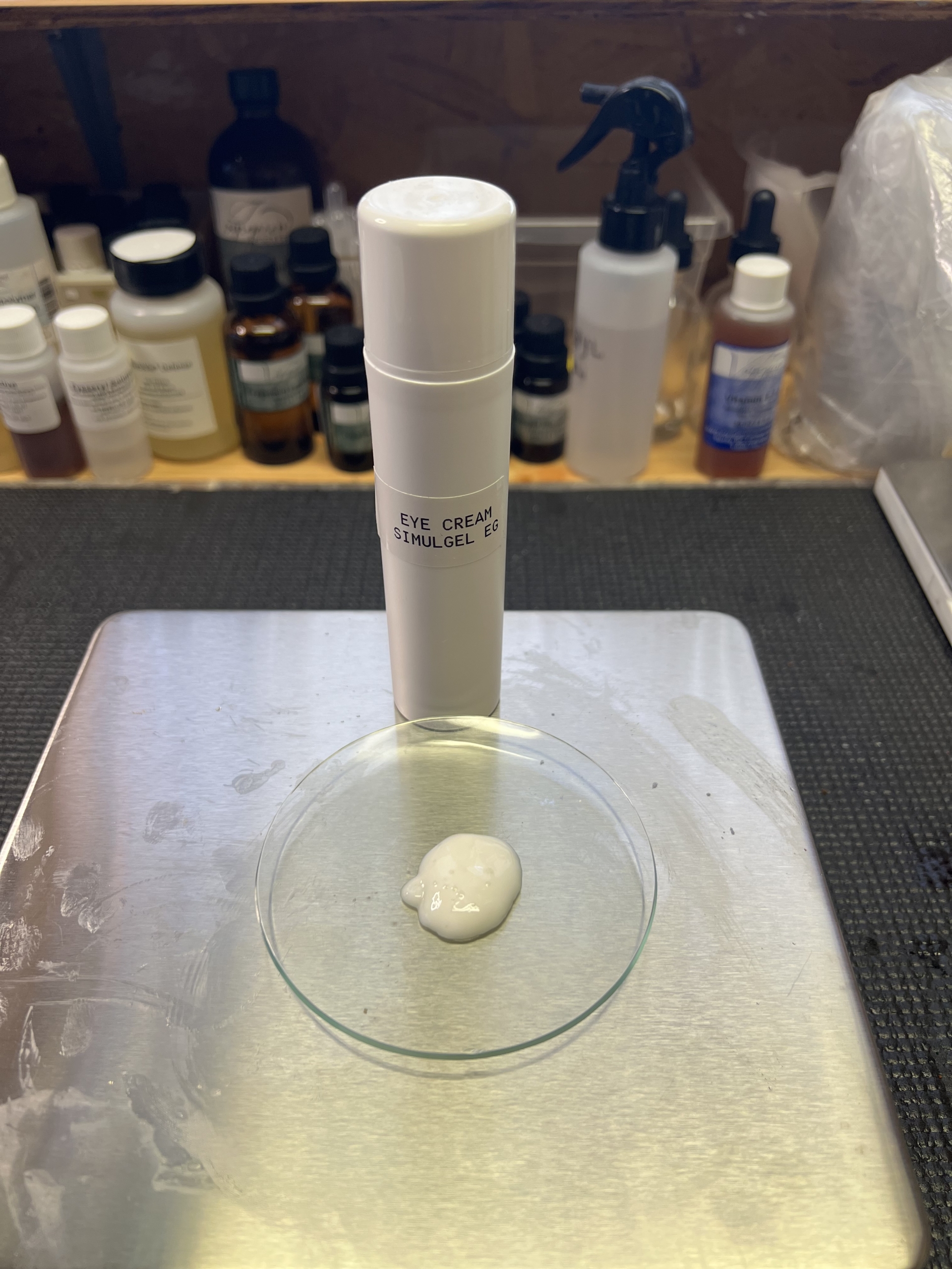 SIMULGEL™️ EG hydrating eye magic gel cream. A white airless pump sits on a digital scale. In front of it is the lotion from the bottle, a white creamy emulsion.