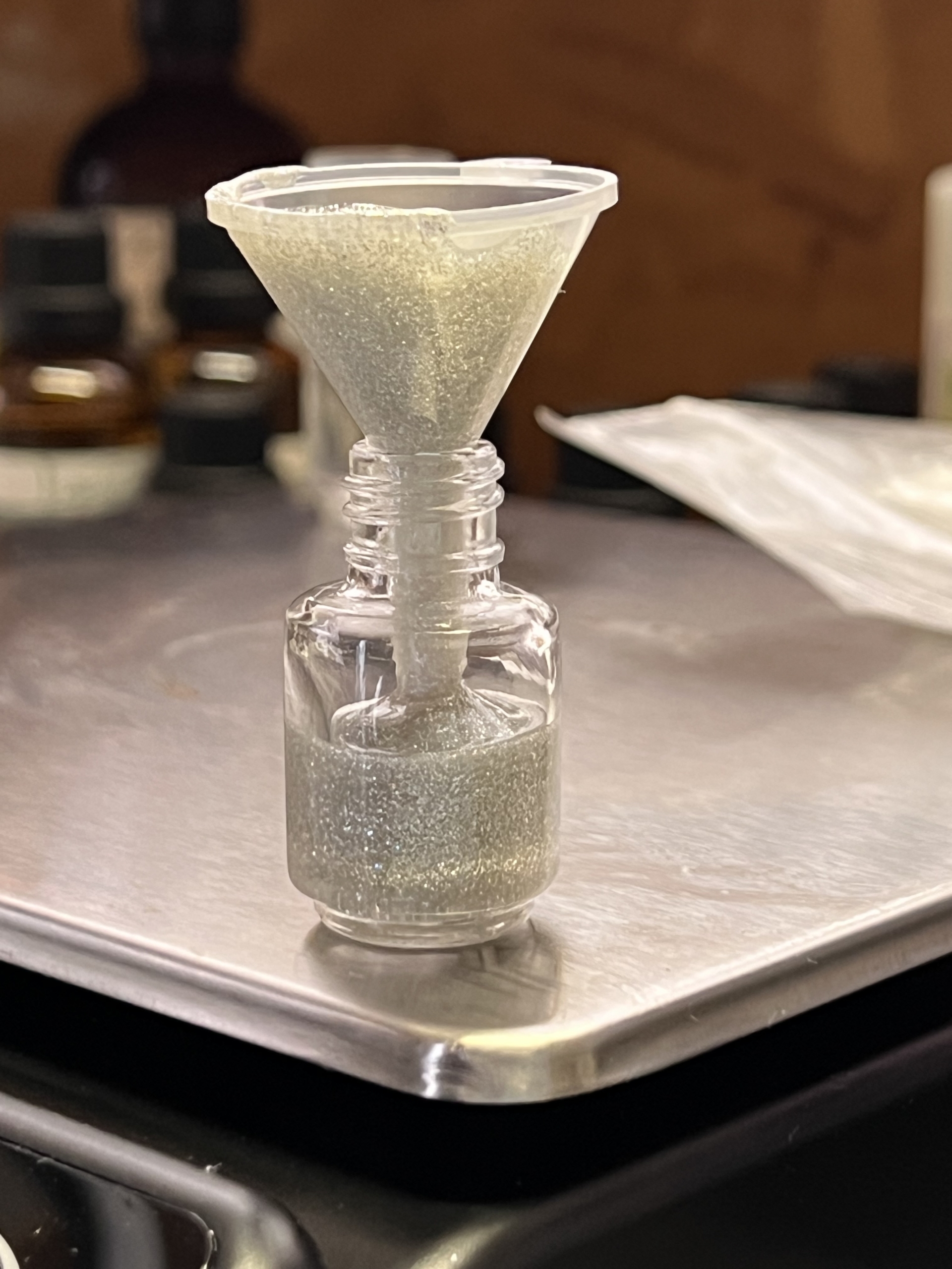 A bottle of glittery nail polish with a funnel in the bottle on the edge of a digital scale