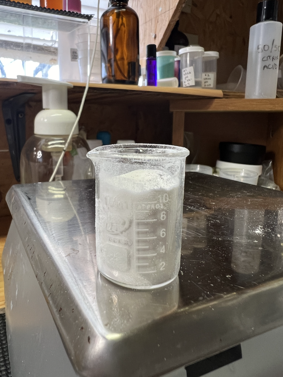 A beaker containing white powder - the emulsifier Eumulgin SG - sits oh the edge of a digital scale