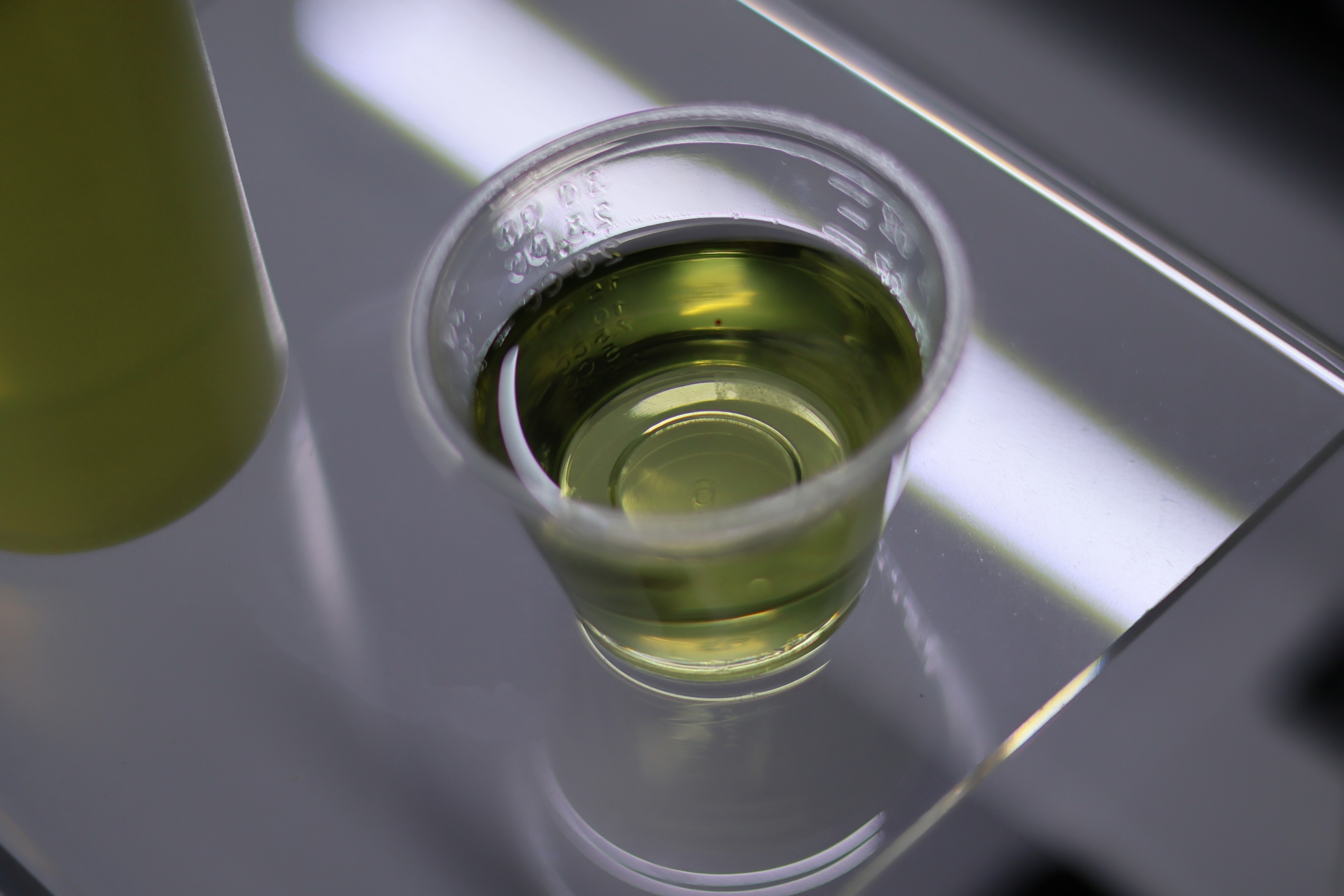 A cup of lightly green coloured grassed oil in a shot glass on top of a clear plastic riser.
