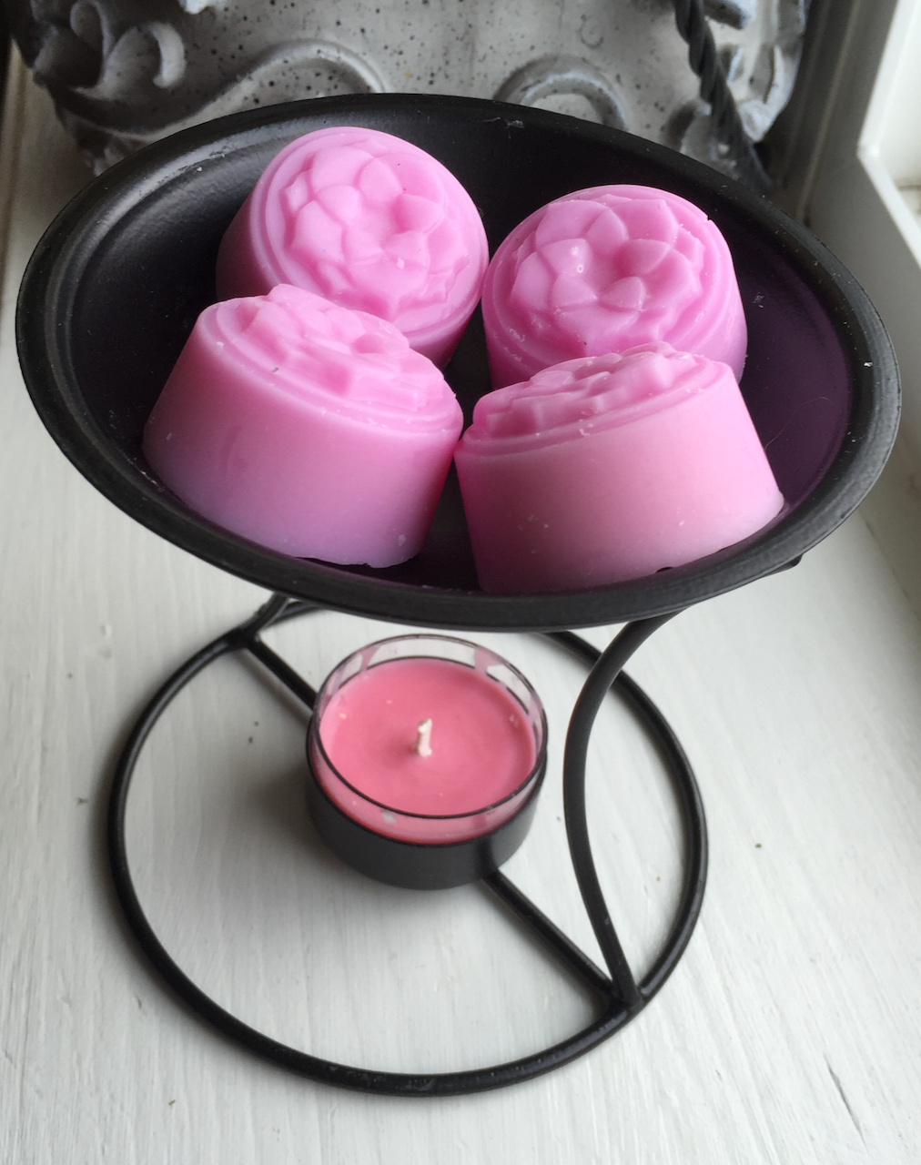 Three pink wax tarts with a lotus motif sit on a black metal wax tart burner with a pink candle underneath