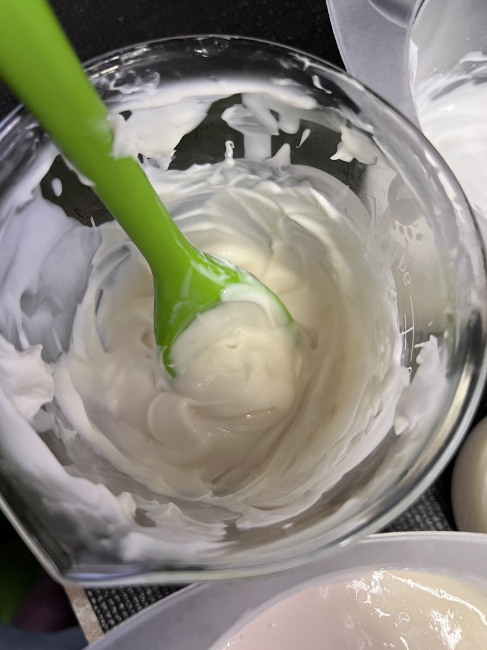 A beaker with a cream coloured emulsion in it. There's a green spoon sticking out of it.