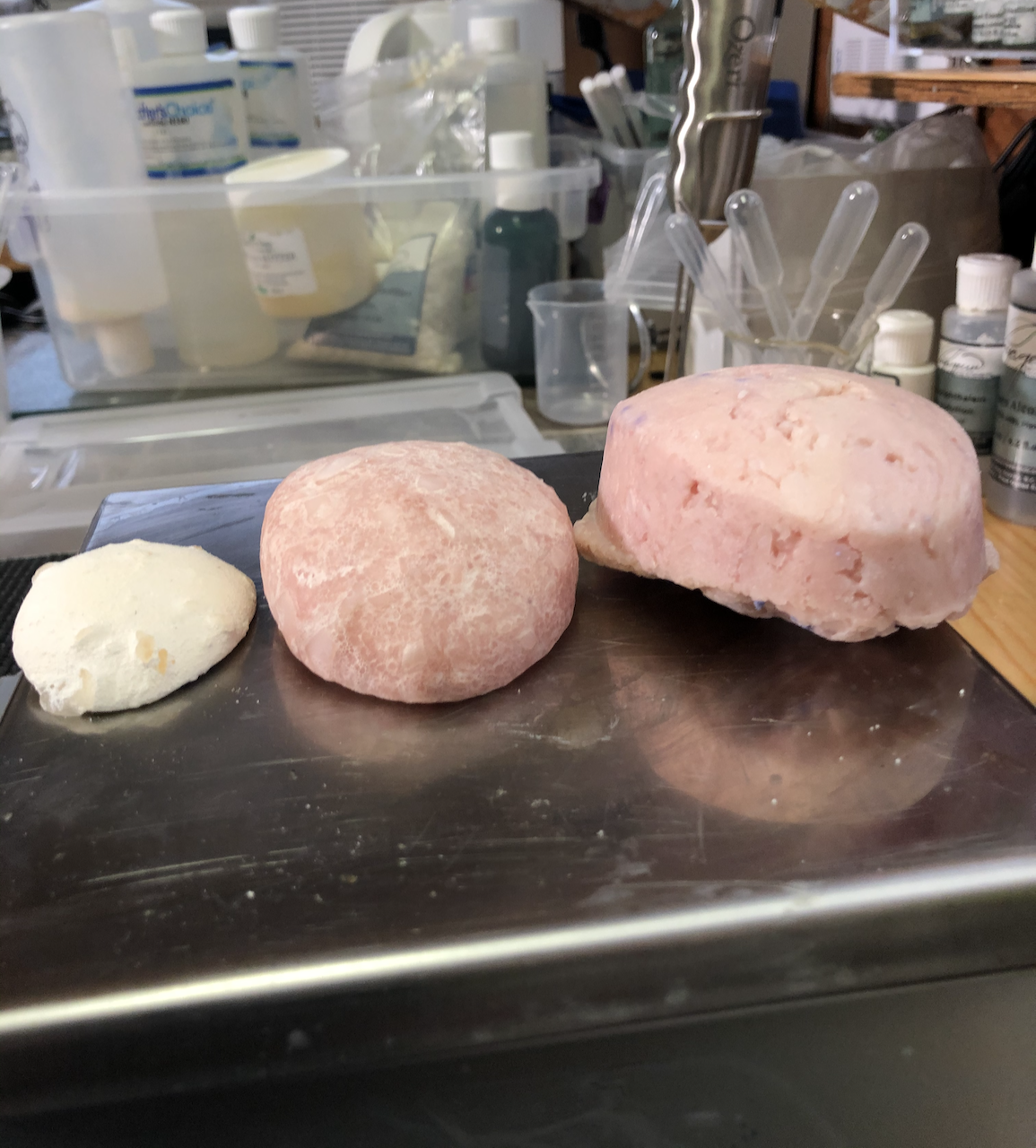 A photo of three shampoo bars on the metal top of a digital scale. From right to left, the largest one is pink; the middle one is pink and smaller because it's been used; the final one is white and it's very small because it's been used a lot.