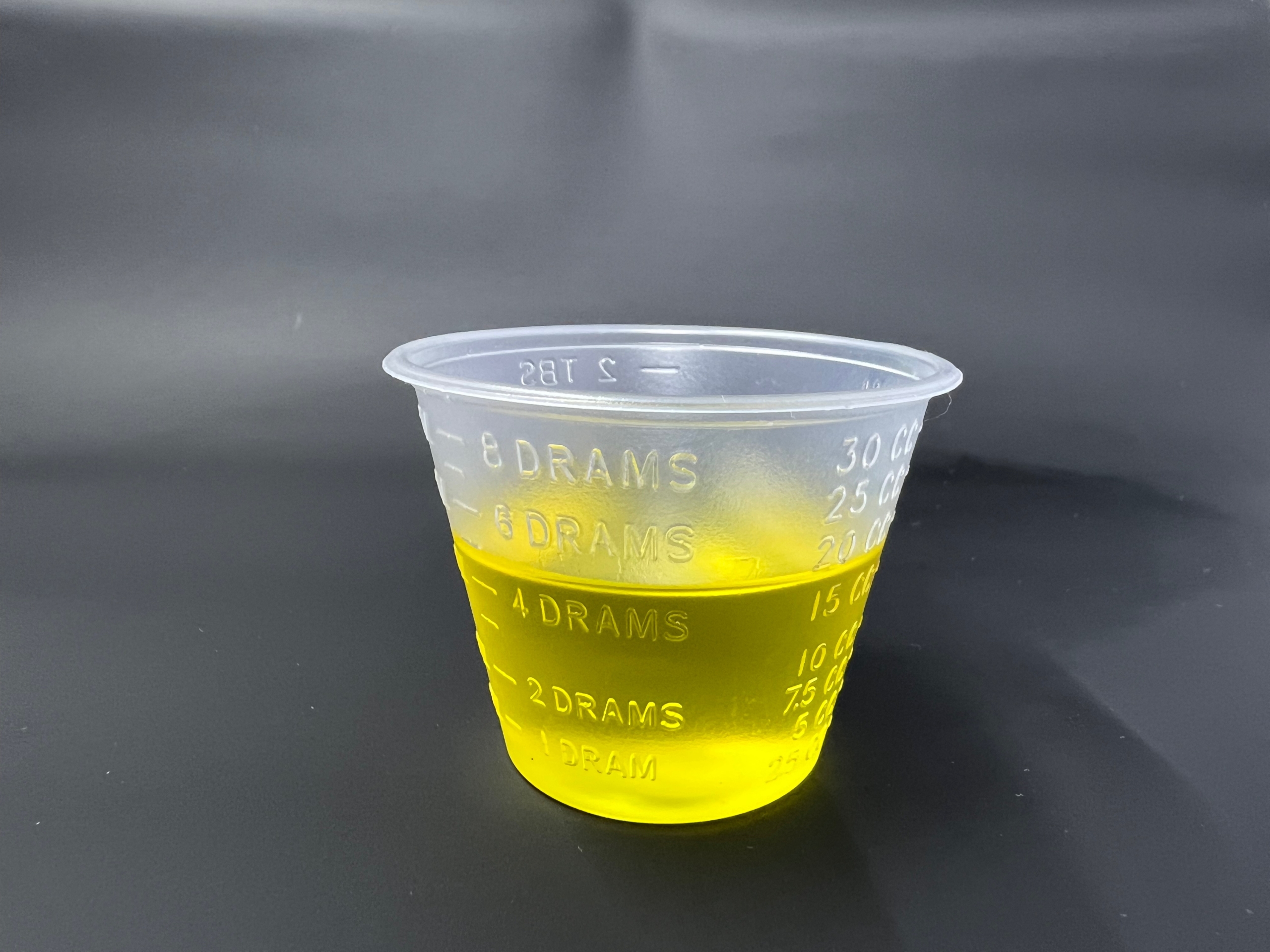 Avocado oil in a plastic shot glass on a black background. It is a yellow, viscous liquid.